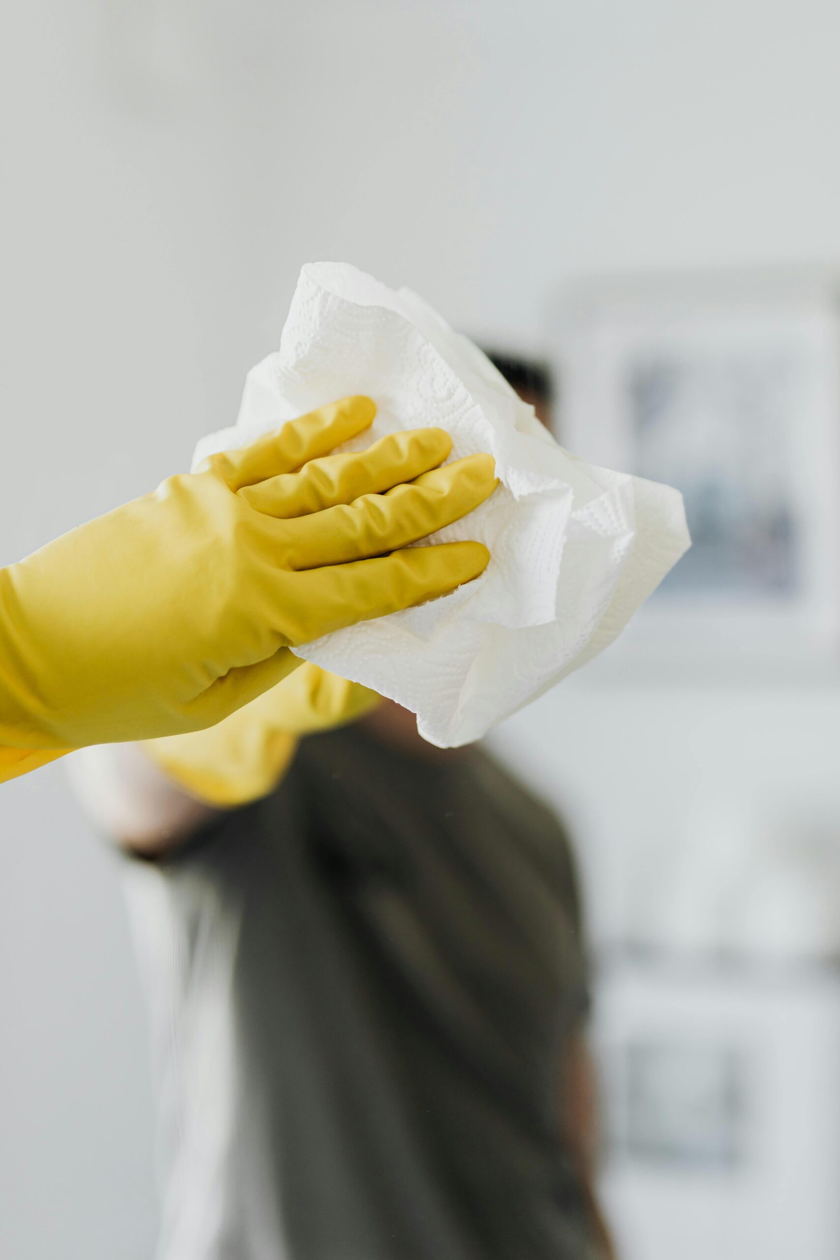 Anonymous male wearing yellow latex gloves and dark t shirt wiping mirror in bathroom with paper napkin